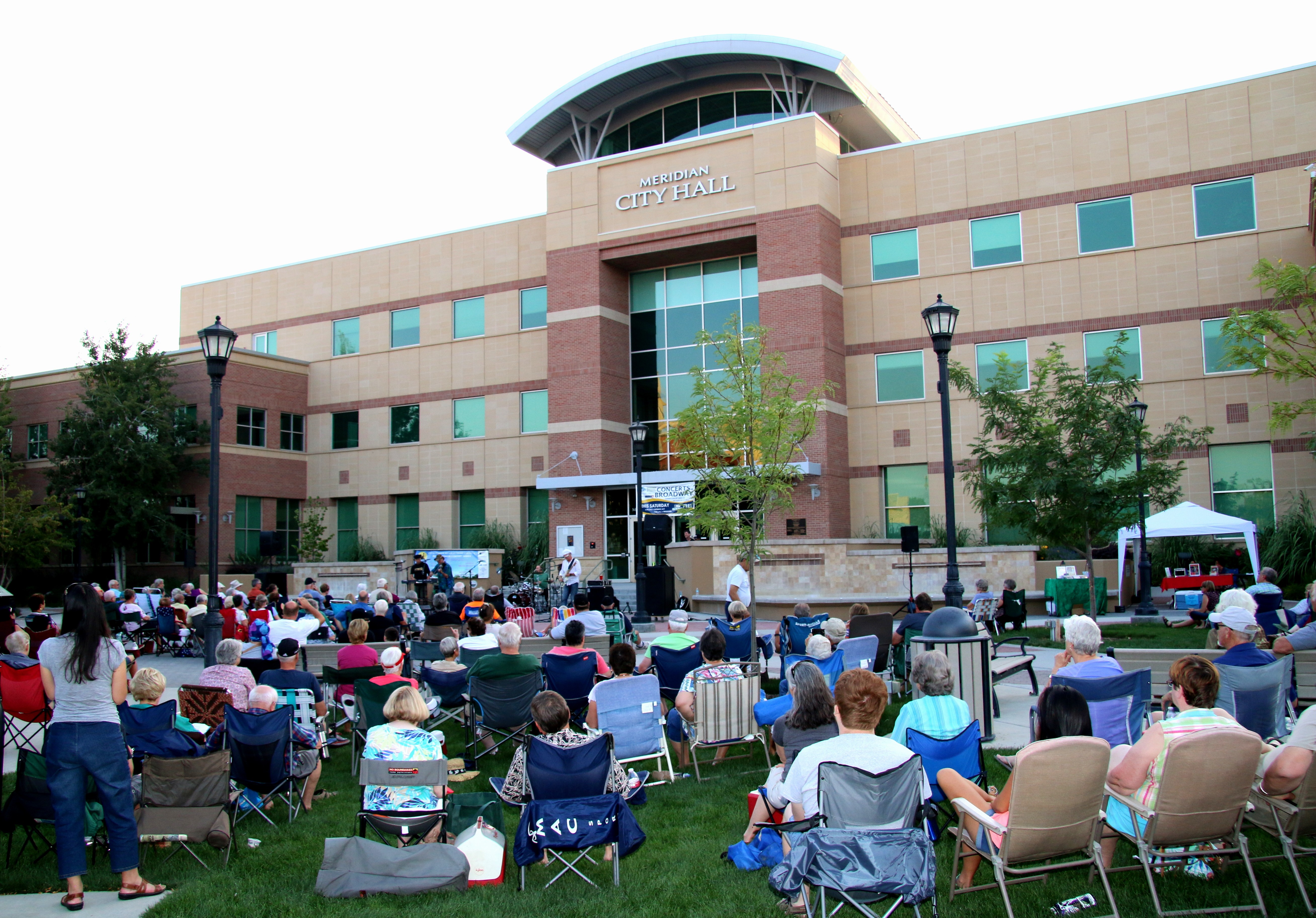 Public in lawn chairs listening to music in from of Meridian's City Hall