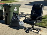 Two trash carts, one extra black and grey trash bags, and an old, black office chair on the curb for City of Meridian Spring Clean Up