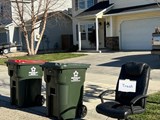 A trash and recycling cart on the curb with an old, black office chair which is considered a bulk item. 