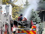 firefighter spraying water from a fire engine at a house fire